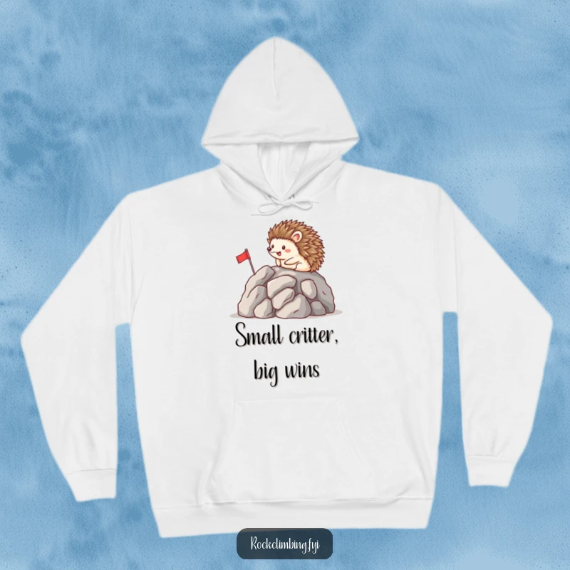 Funny hoodie depicting a happy hedgehog planting a tiny flag on a mountain peak, offering warmth and humorous celebration of success.